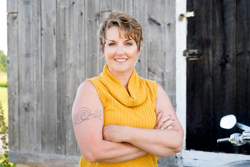 Sable Hart, fantasy romance author, smiling outdoors in front of a rustic wooden barn.